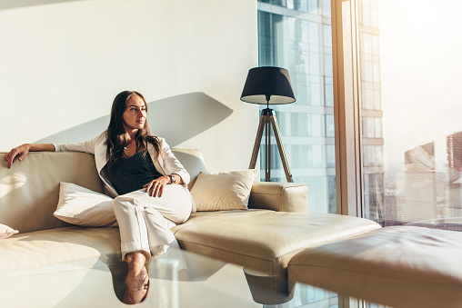 Portrait of successful businesswoman wearing elegant formal suit sitting on leather sofa relaxing after work at home.