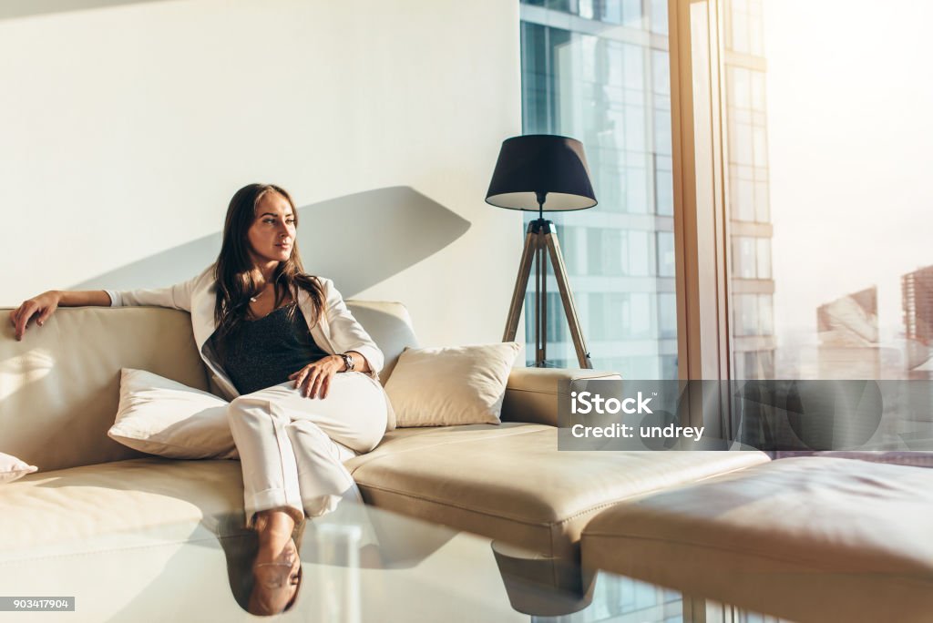 Portrait of successful businesswoman wearing elegant formal suit sitting on leather sofa relaxing after work at home Portrait of successful businesswoman wearing elegant formal suit sitting on leather sofa relaxing after work at home. Luxury Stock Photo