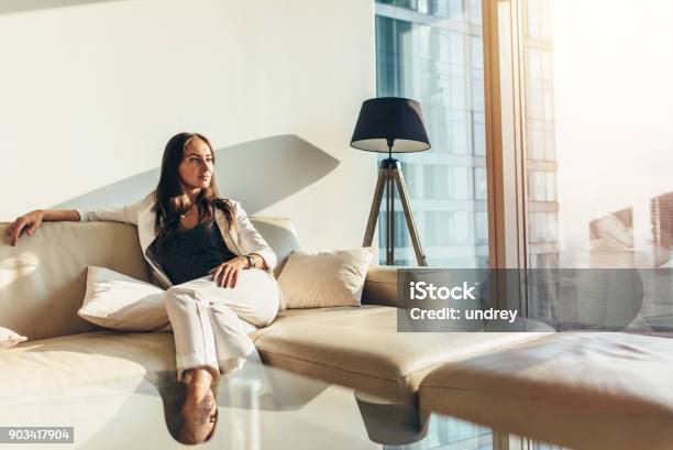 Portrait Of Successful Businesswoman Wearing Elegant Formal Suit Sitting On Leather Sofa Relaxing After Work At Home Stock Photo - Download Image Now