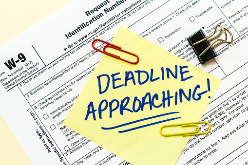 A W9 tax form with DEADLINE APPROACHING written on a yellow sticky note.