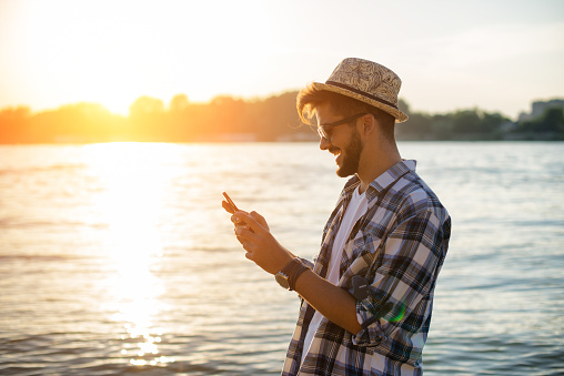 Young man is using his phone on  beach in sunset
