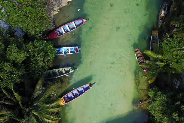 Aerial shot of White River, Ocho Rios, Jamaica with 4 colorful fishing boat moored in a small fishing settlement. Fishes are visible through the clear waters.