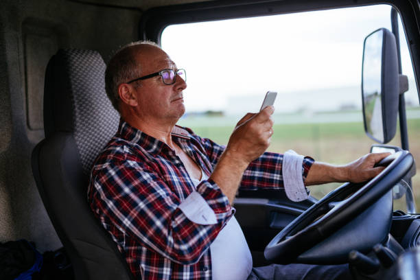 Driving a truck Senior man driving a truck and texting on a mobile phone. semi truck photos stock pictures, royalty-free photos & images