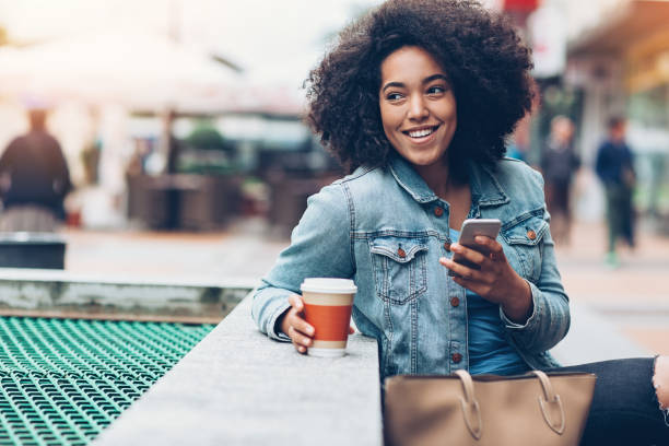 Messaging outdoors in the city Young African ethnicity woman holding smart phone outdoors denim jacket stock pictures, royalty-free photos & images