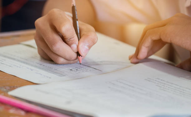 istock Front view Asian Students, undergraduate holding pencil writing on multiple-choice quizzespaper answer sheet and sitting on old lecture chair in final exam classroom, Education  literacy concept. 903491414