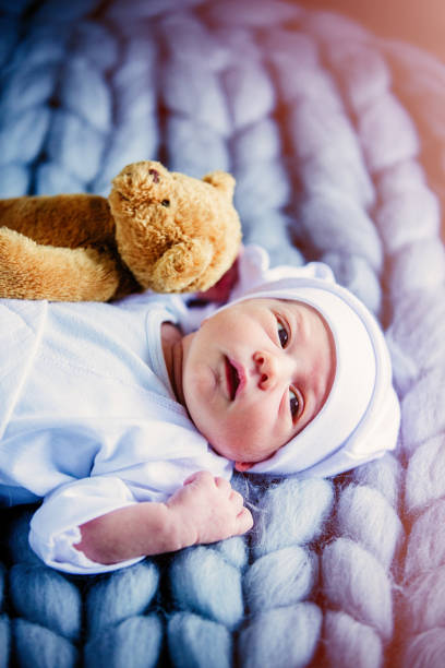istock little baby wearing a white clothes and hat with taddy bear 903495178
