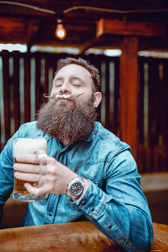 Handsome Bearded Hipster Person Drinking Beer In Pub and Enjoying