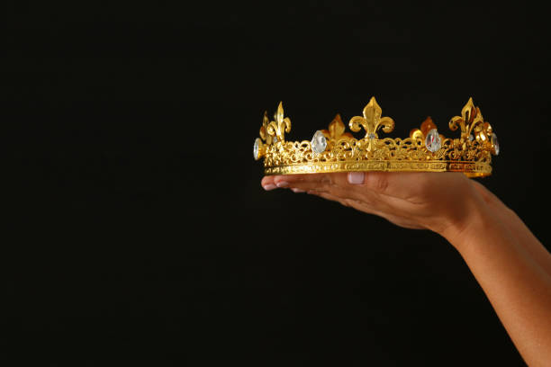 istock Woman's hand holding a crown for show victory or winning first place over black background. 903505672