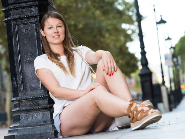 Young stylish woman sitting near lamp post on summer city street