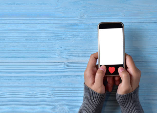 istock Female hands holding white blank cell phone screen with red hearts on home button. 903513324