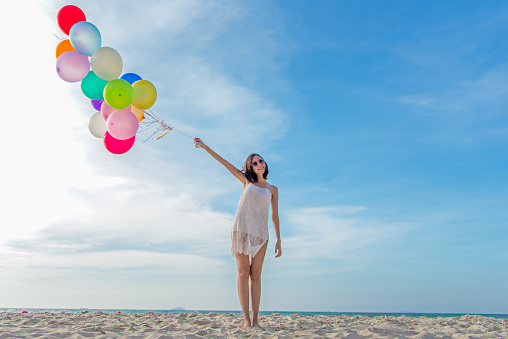Smiling lifestyle asian woman hand holding balloon on the beach.  Relax and Enjoy in summer holiday.  Summer and Travel Concept