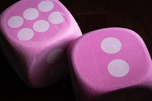 horizontal macro image of two large pink dice with white dots.