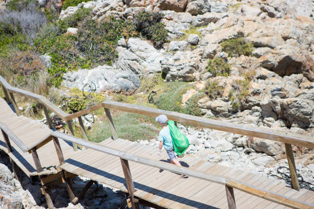 A young boy carries a green plastic bag and picks up rubbish for recycling along the beautiful coast