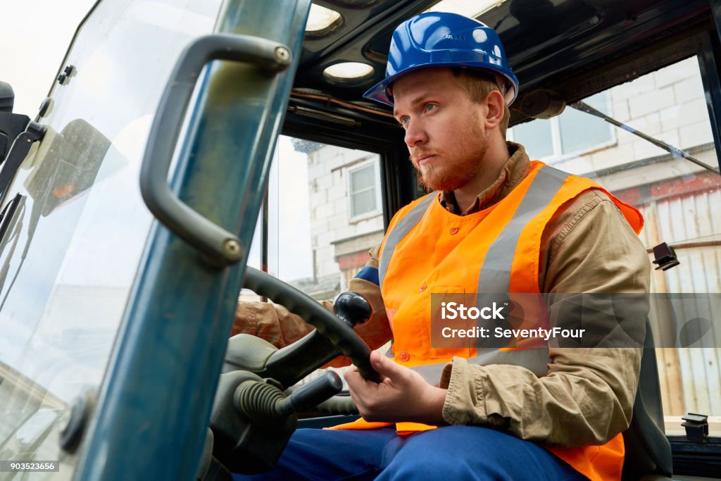 Bearded Worker Driving Lift Truck Confident bearded worker wearing protective helmet and reflective vest driving lift truck while working in port warehouse, portrait shot Crane - Machinery Stock Photo