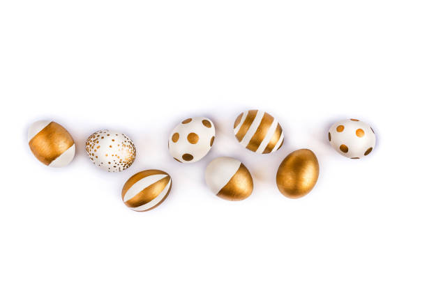 Top view of easter eggs colored with golden paint in differen patterns. Various striped and dotted designs. White background. Copy space.