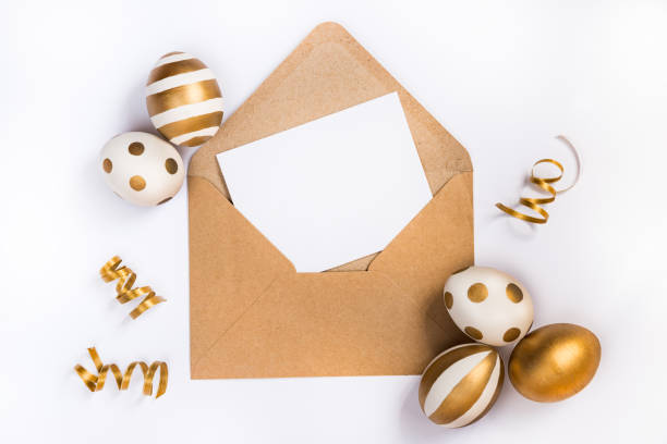 istock Easter festive decoration. Top view of easter eggs colored with golden paint in differen patterns and empty mock-up card in a kraft envelope. Various striped and dotted designs. White background. 903527362