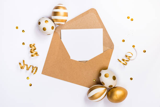 istock Easter festive decoration. Top view of easter eggs colored with golden paint in differen patterns and empty mock-up card in a kraft envelope. Various striped and dotted designs. White background. 903527390