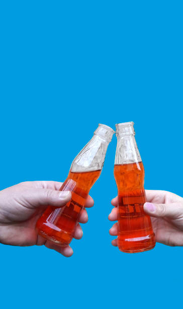 istock Two hands holding a drink and making toast, clinking bottles with lemonade or beer, isolated on blue background 903533982