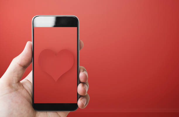 istock Hand holding Mobile smart phone red heart screen, on red background 903541904