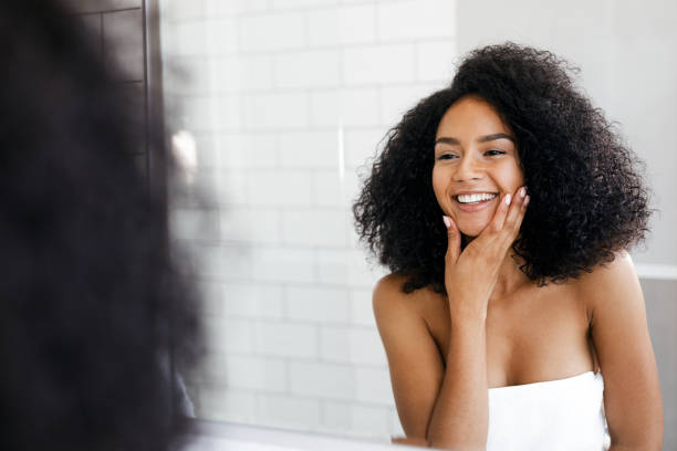 istock Shot of a cheerful woman touching her face with her hand while looking at reflection in a mirror 903545110
