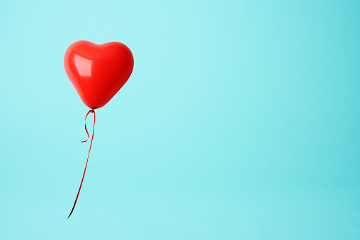 Red heart shape balloon against blue background with copy space.