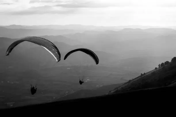 Photo of Some paragliders flying over a mountain scenery, with some faint sunrays in the background