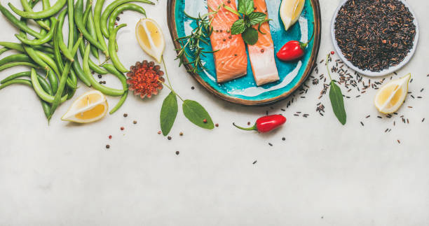 Raw salmon steaks with vegetables, rice and greens on plate