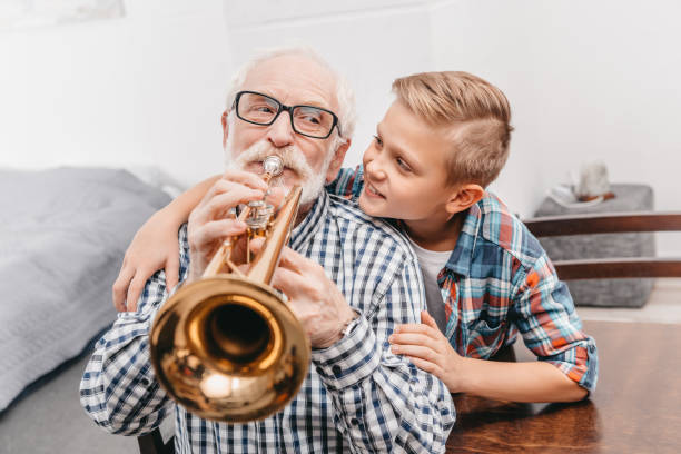 Grandfather playing trumpet Grandfather playing trumpet while smiling boy is hugging him from behind man trumpet stock pictures, royalty-free photos & images