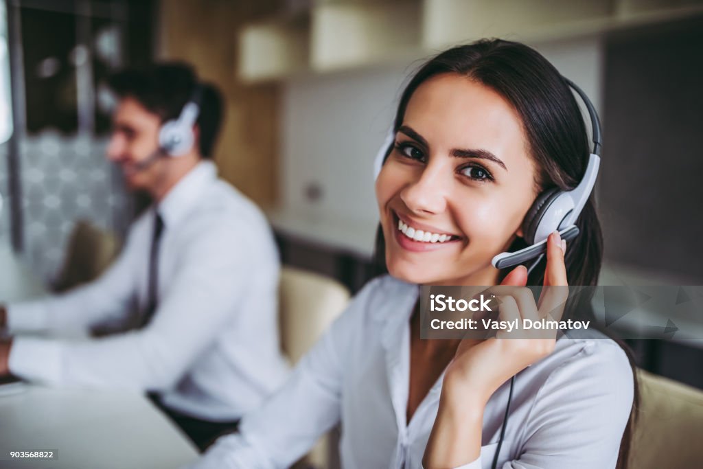 Call center workers. How can I help you? Beautiful call center workers in headphones are working at modern office. Customer Service Representative Stock Photo