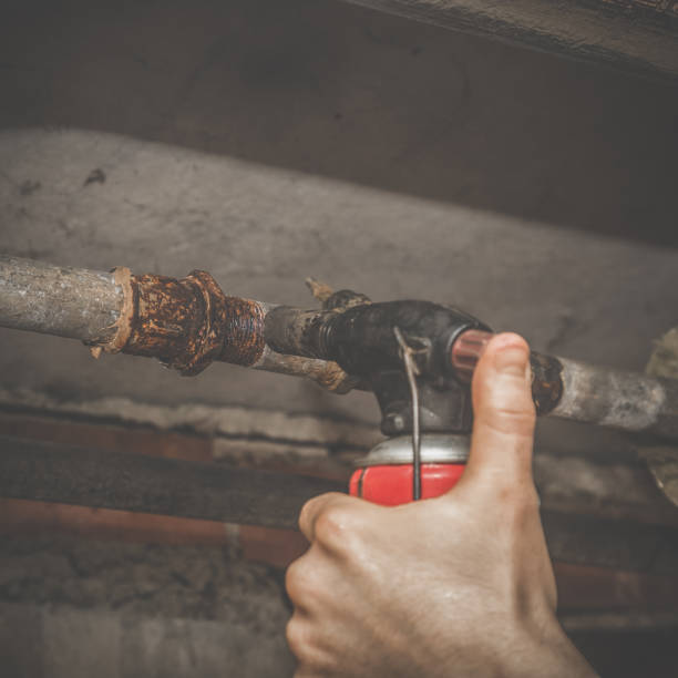 istock Plumber using gas burner for warming old rusty pipe before unscrewing it. Dirty job in the basement. Plumbing concept. Vintage style. 903569372