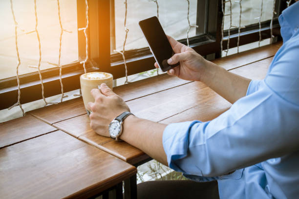 istock Close up of men hands holding touching mobile phone with blank copy space for your text message on wood in the cafe with light Sunset,Vintage tone.Selective focus 903578366
