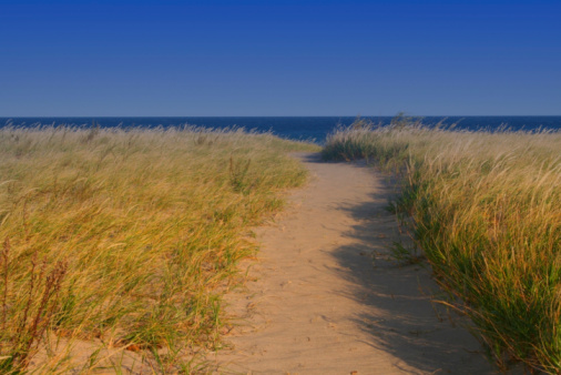 Summer beach landscape with wicker chairs, high grass dunes, and the North Sea water, on Sylt island, Germany. Sunny summer vacation context.