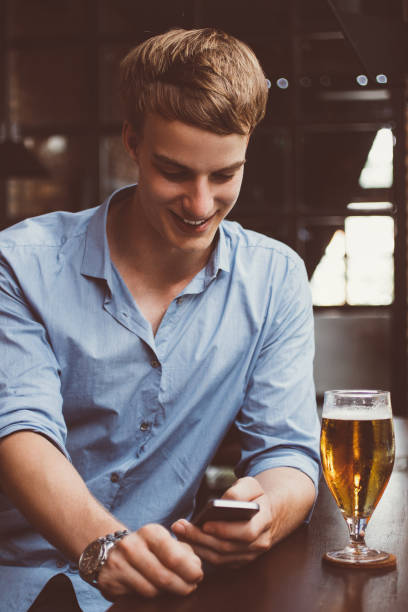 istock Smiling Young Man Texting on Smartphone in Pub 903583920