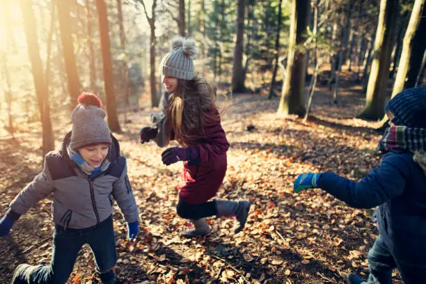 Winter without snow. Happy kids are playing tag in forest.  It looks more like autumn because there is no snow.
