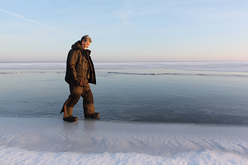 Elderly man in warm clothes walking on the ice of a frozen river at sunset, Ob reservoir, Siberia, Russia