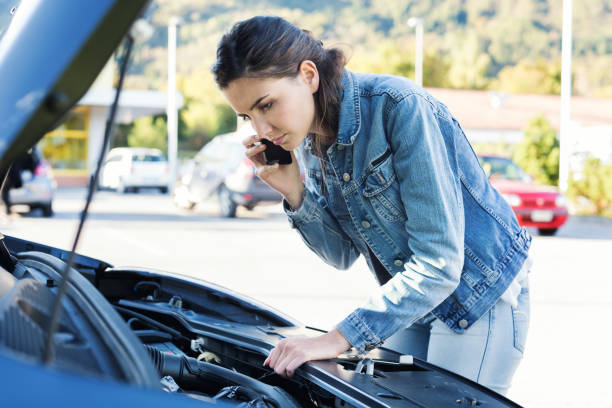 Woman calling car assistance Young woman calling a car assistance service with her smartphone, her car has broken down vehicle breakdown stock pictures, royalty-free photos & images