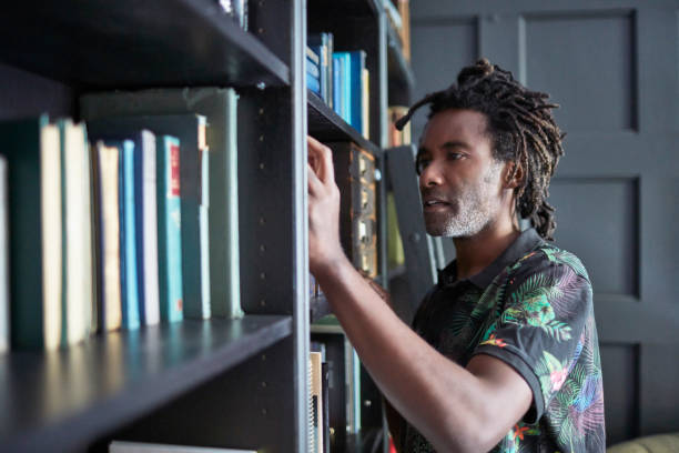 istock Man searching for book in shelves at home 903597572