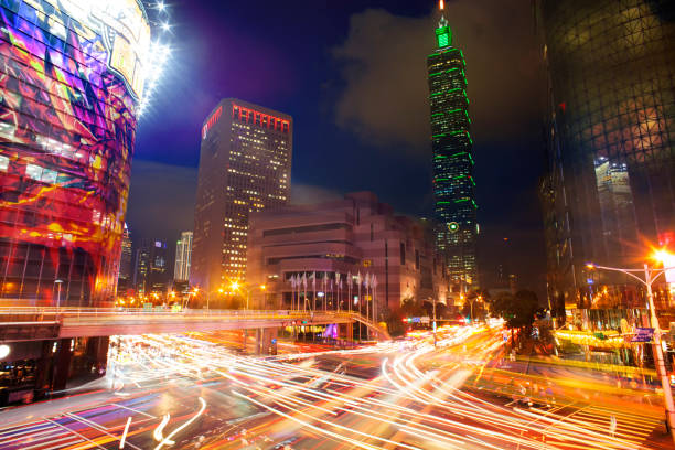 light trails from vehicle traffic streak across a busy intersection in front of Taipei 101 THe light trails from vehicle traffic streak across a busy intersection in front of Taipei taipei photos stock pictures, royalty-free photos & images