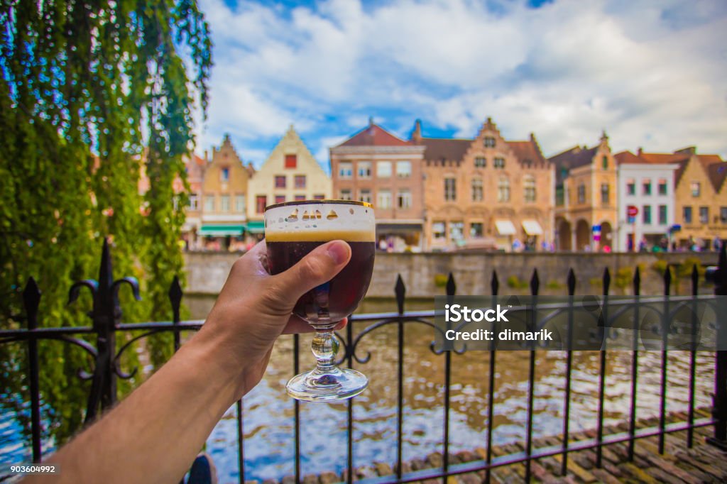 Hand with beer glass in Brugge Full glass of beer on Brugge cityscape background. Hand with beer glass in Bruges, Belgium. Belgium Stock Photo