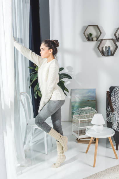 side view of beautiful pensive young woman looking at window at home