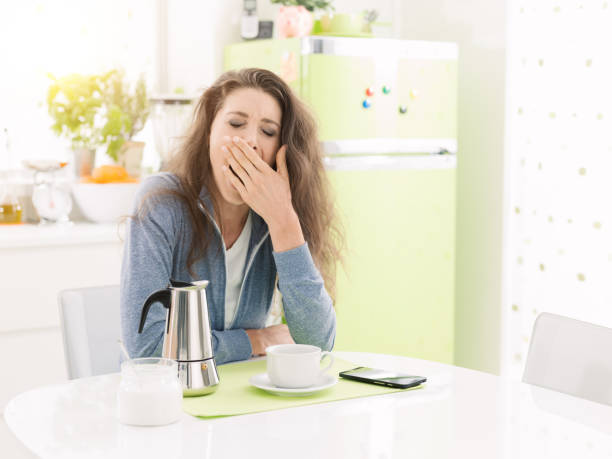 donna stanca che fare colazione a casa - yawning women drink coffee cup foto e immagini stock