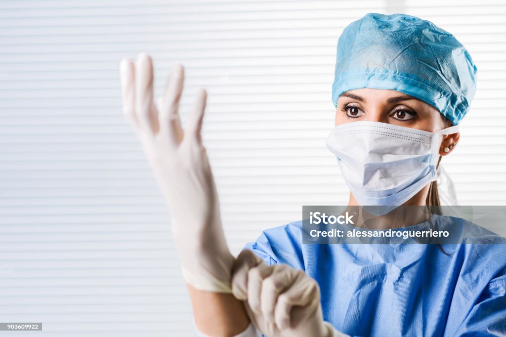 Female doctor Surgeon putting on surgical gloves Portrait of Female doctor Surgeon in blue scrubs putting on surgical gloves Glove Stock Photo