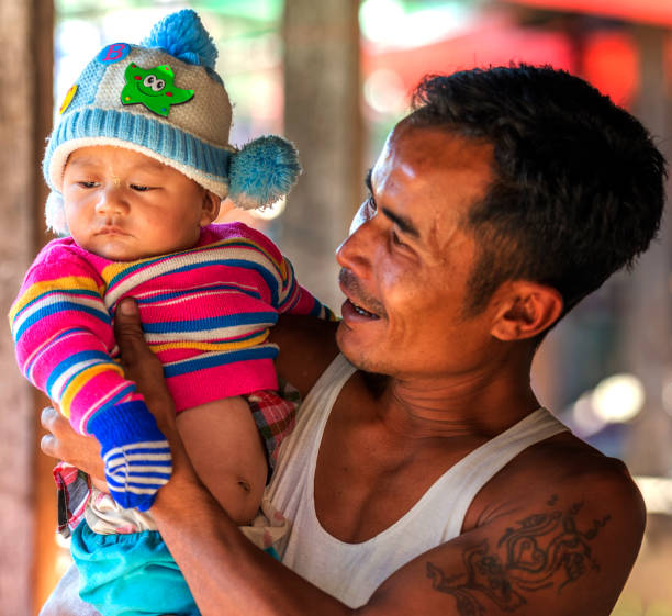 hombres sosteniendo a su bebé en sus brazos y sonriendo en un mercado local, inle, myanmar - bagan myanmar burmese culture family fotografías e imágenes de stock