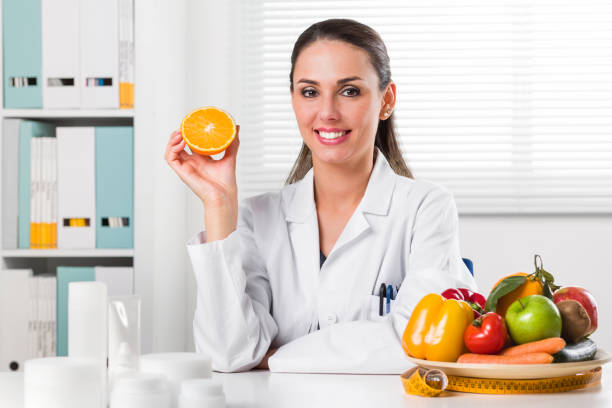 nutrizionista donna che tiene una fetta d'arancia - orange uniform foto e immagini stock