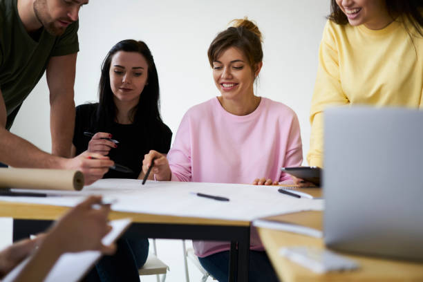 istock Smiling male and female students creating coursework project together in friendly atmosphere, crew of skilled casually dressed designers drawing blueprint making accountings sitting in office indoors 903621722