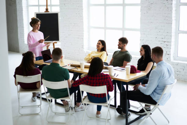 istock Cheerful professional female coach making brainstorming session with staff members using teambuilding concept, crew of smiling male and female students enjoying training lesson with creative teacher 903621748