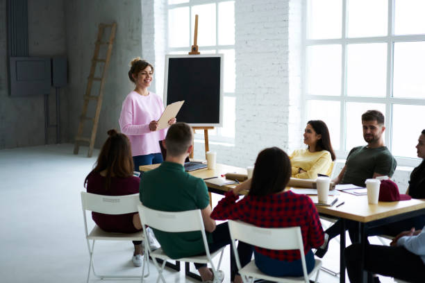 istock Cheerful female coworker making presentation of creative project speaking about concept and strategies standing in front of auditory, skilled coach explaining to employee details of collaboration 903622442
