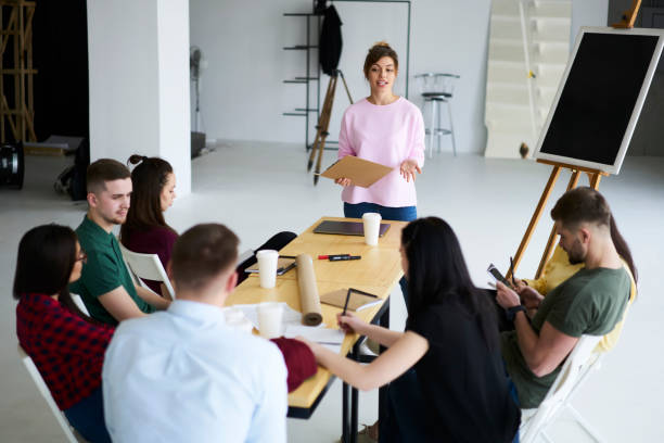 istock Charming young female teacher making presentation during lesson in university standing near board, business coach explaining successful strategies for setting up startup project for trainees crew 903623980