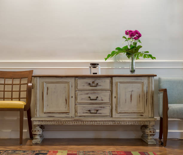 vintage in legno fuori la credenza bianca, vaso di vetro con fiori rossi, due sedie su parete bianca e pavimento in parquet in legno - sideboard foto e immagini stock