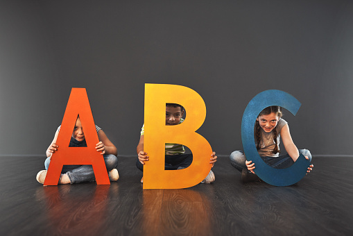 Studio portrait of a diverse group of kids holding up letters of the alphabet against a gray background